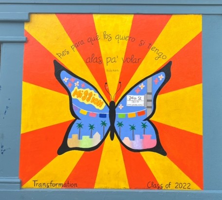 A colorful school mural of a butterfly with imagery of the Mission neighborhood of San Francisco in the wings. Writing in Spanish and English surrounds the butterfly: “Pies para qué los quiero si tengo alas pa’ volar. Transformation. Class of 2022”