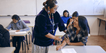 A teacher speaking with a student in a classroom.