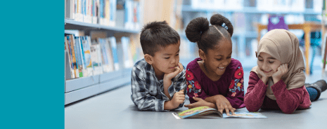 Multi-ethnic preschool students reading a book on a library floor